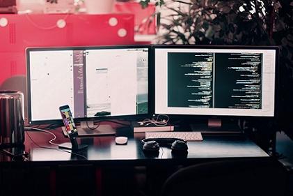 Two computer monitors, at office desk, displaying programming code