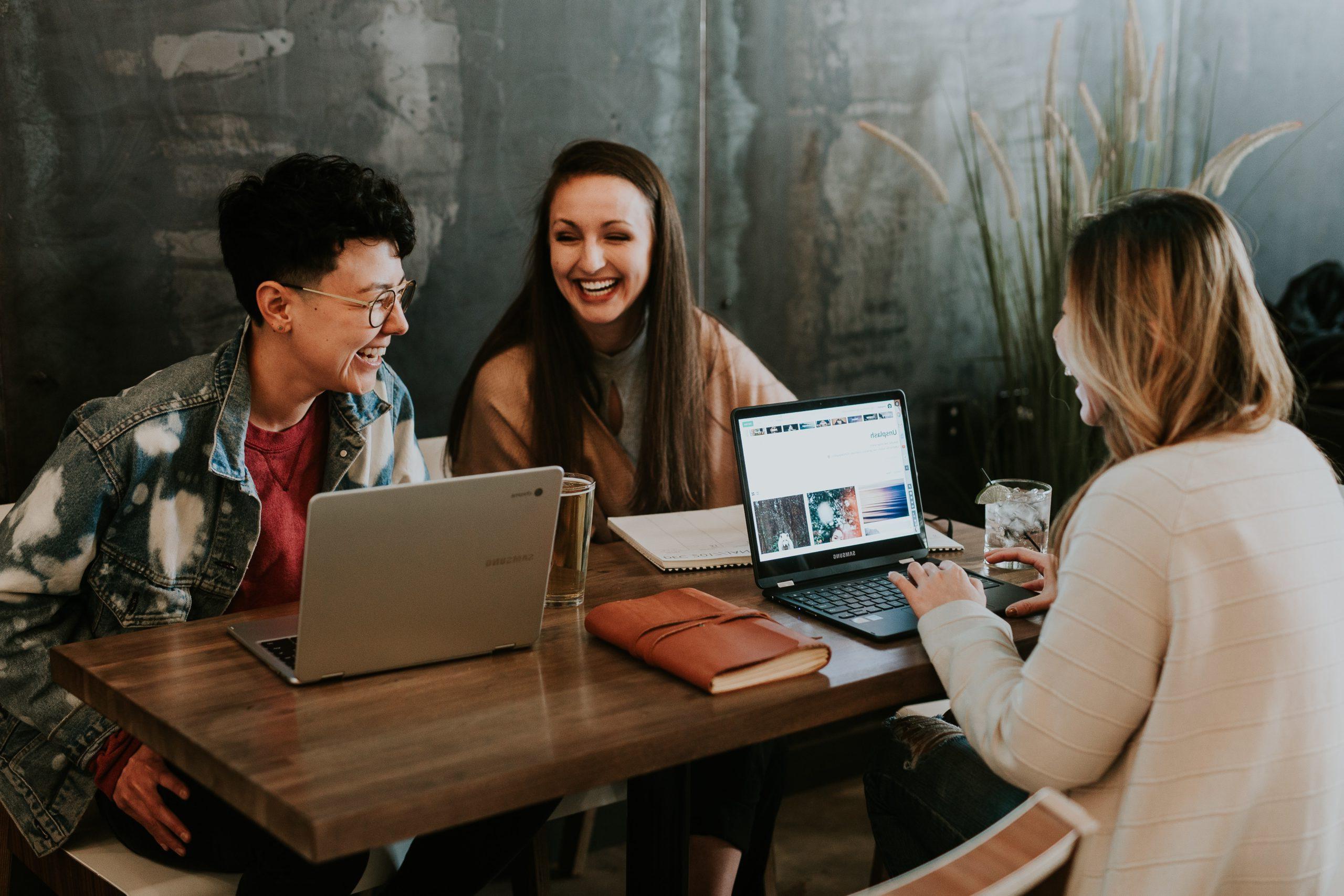 Three people laughing 和 sitting at a table with their laptops